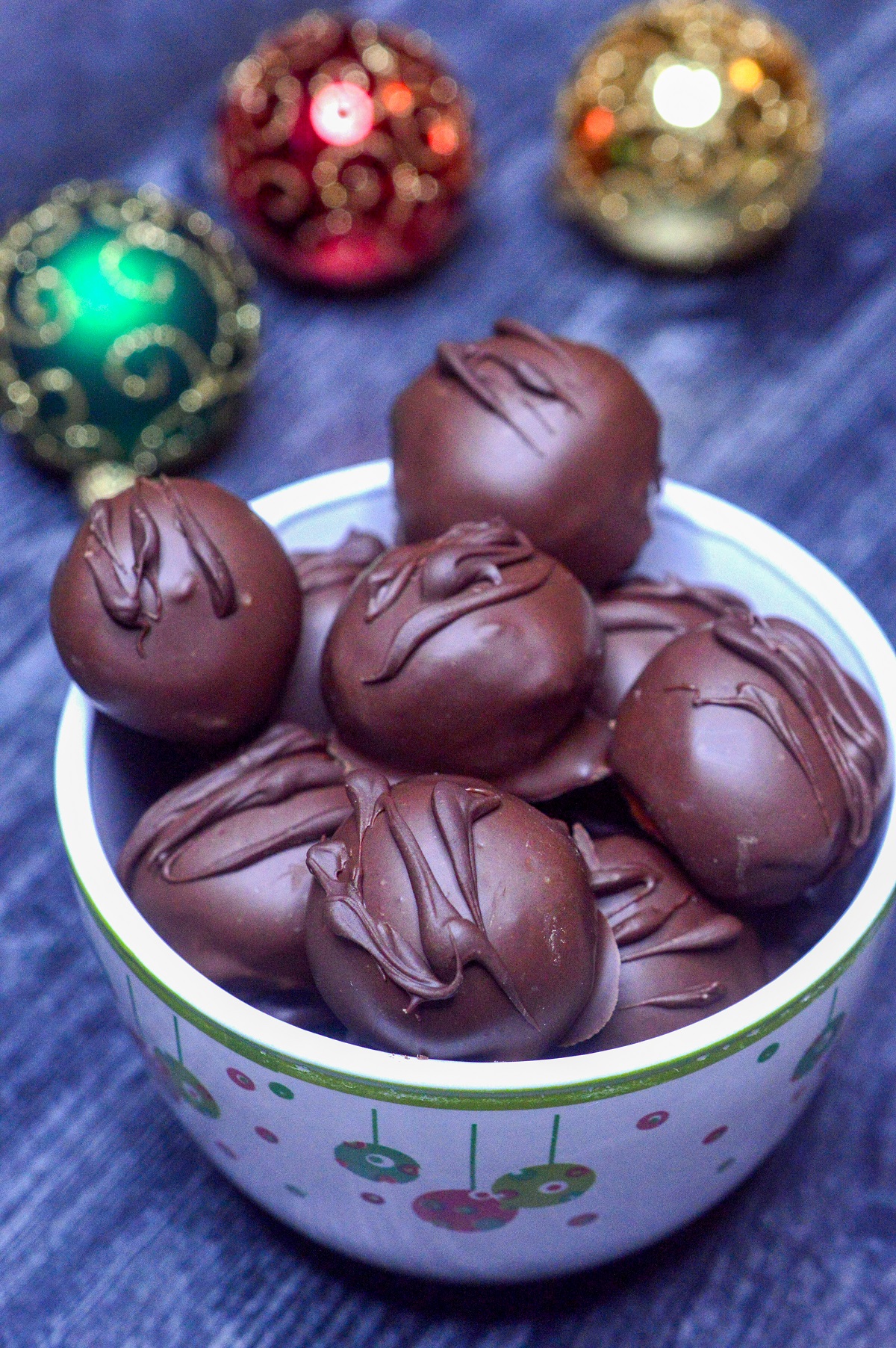 Chocolate Covered Peanut Butter Balls also called PEanut Butter Truffles. Peanut Butter Balls dipped in chocolate Shown in a christmas bowlk with Christmas ornaments oin backround.