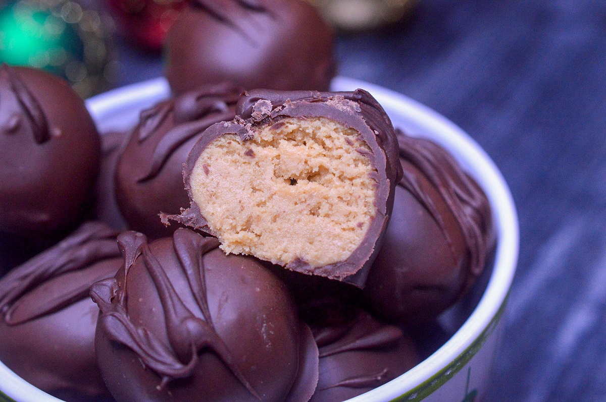 Chocolate Covered Peanut Butter Balls also called PEanut Butter Truffles. Peanut Butter Balls dipped in chocolate Shown in a bowl with one canbdy cut in half.