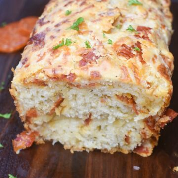 This super easy Cheesy Pepperoni Bread is an easy & tasty quick bread recipe that can be made as bread or as drop biscuits. SO good! Shown a loaf sliced open on a wood cutting board.