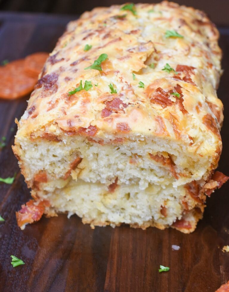 This super easy Cheesy Pepperoni Bread is an easy & tasty quick bread recipe that can be made as bread or as drop biscuits. SO good! Shown a loaf sliced open on a wood cutting board.