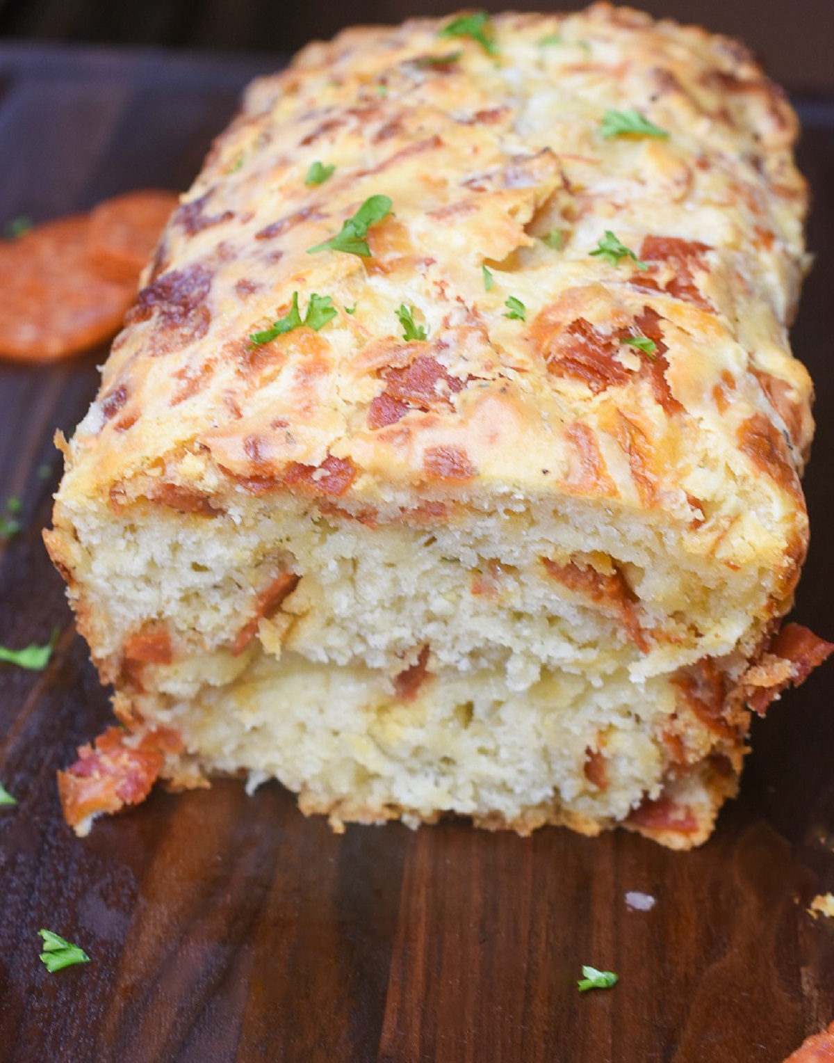 Pepperoni Quick Bread recipe. Shown a baked quick bread recipe of Pepperoni Bread sliced open on a wood cutting board.