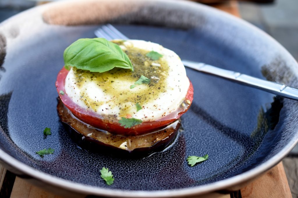 Grilled Eggplant Tomato Mozzarella with pesto in a black bowl topped with basil leaf