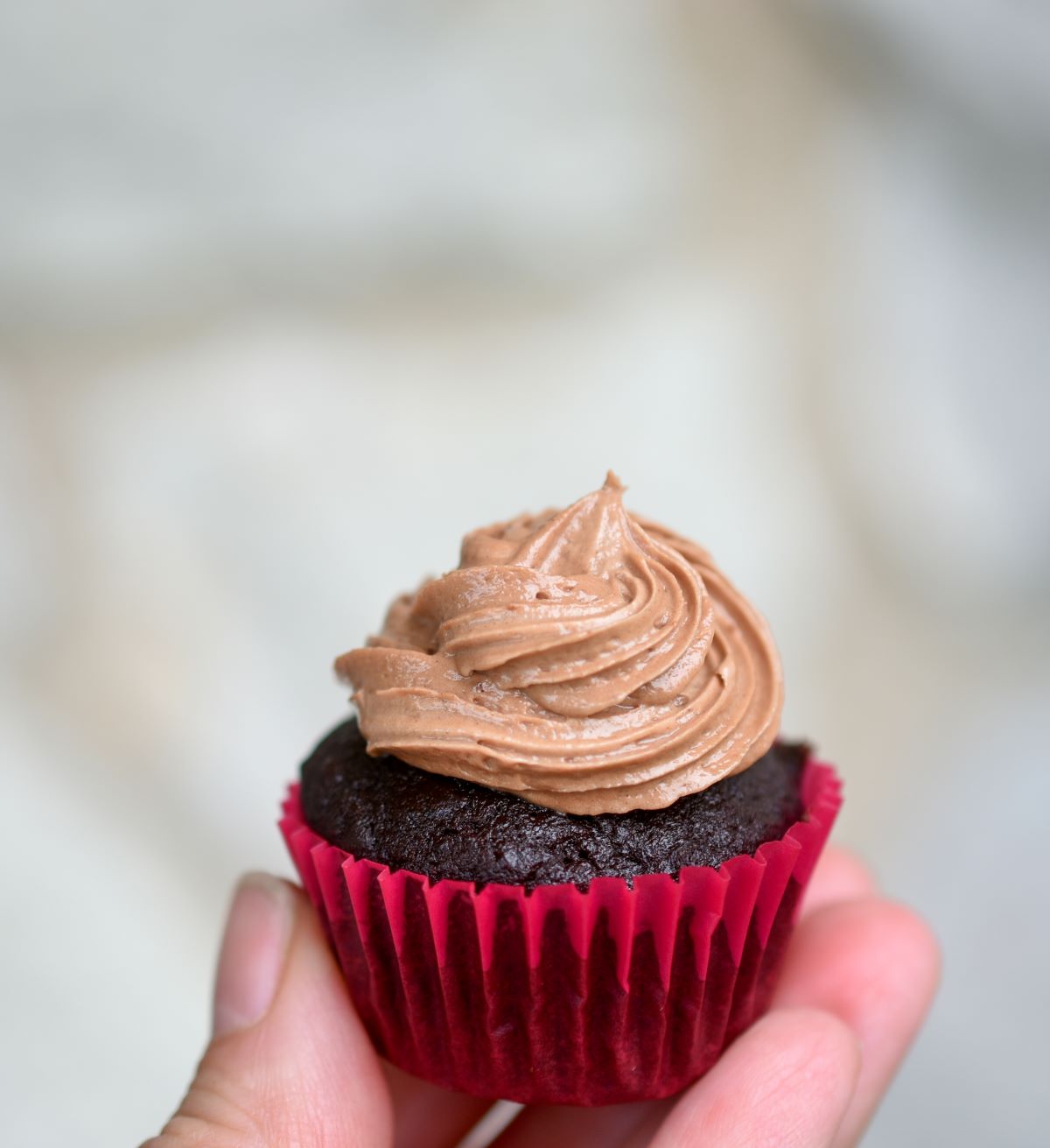 One mini Chocolate Banana Cupcake topped with Chocolate buttercream frosting, held in a hand with a hot pink cupcake liner.