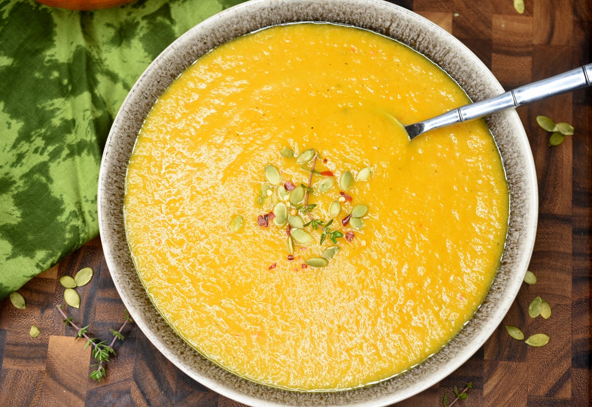 Detox Pumpkin Soup in a bowl with spoon and pepitas on top as garnish