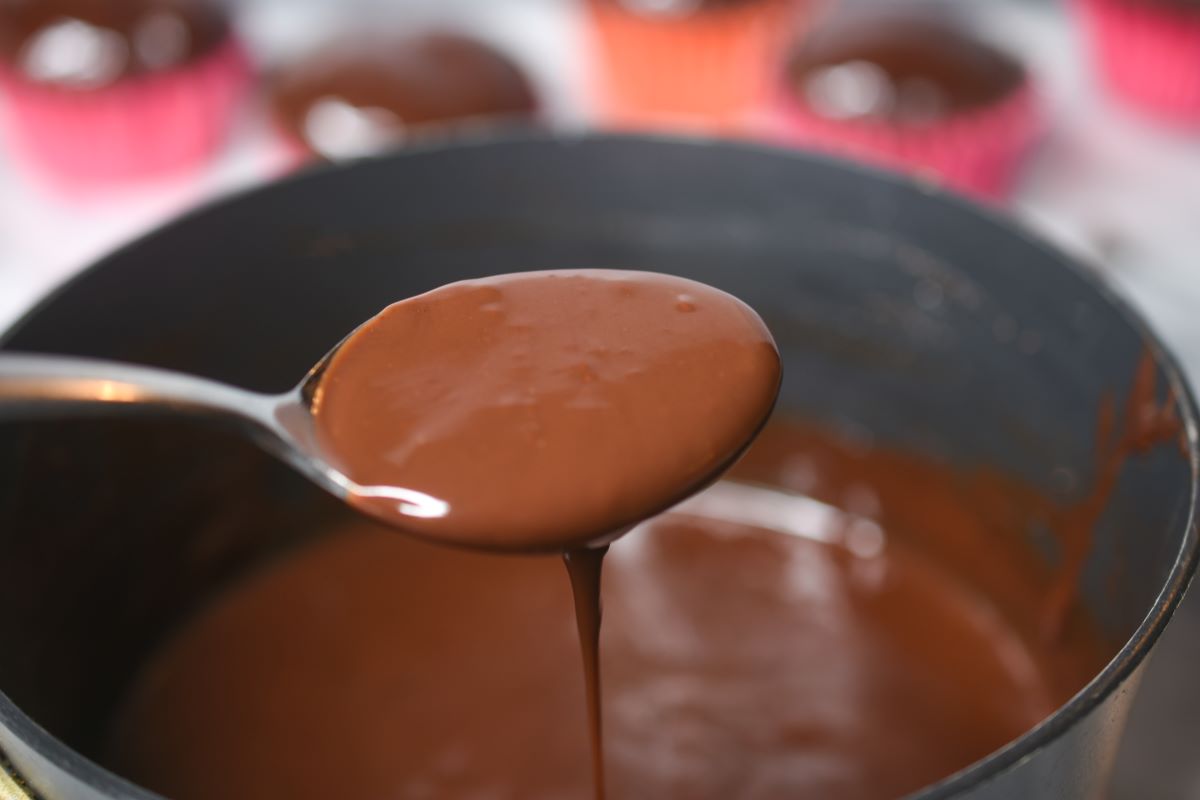 Chocolate Ganache in a pot ready to be used for cupcakes. Chocolate ganache dripping off of spoon.