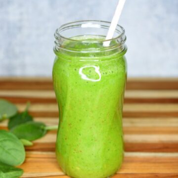 BEST Green Smoothie Recipe. 4 Ingredient Green Smoothie recipe. Shown in a tall glass mason jar with straw. baby spinach leaves in background.