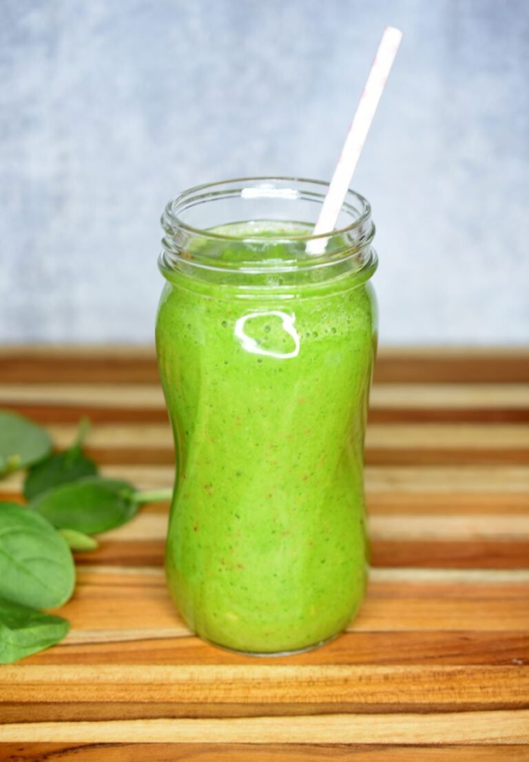 BEST Green Smoothie Recipe. 4 Ingredient Green Smoothie recipe. Shown in a tall glass mason jar with straw. baby spinach leaves in background.
