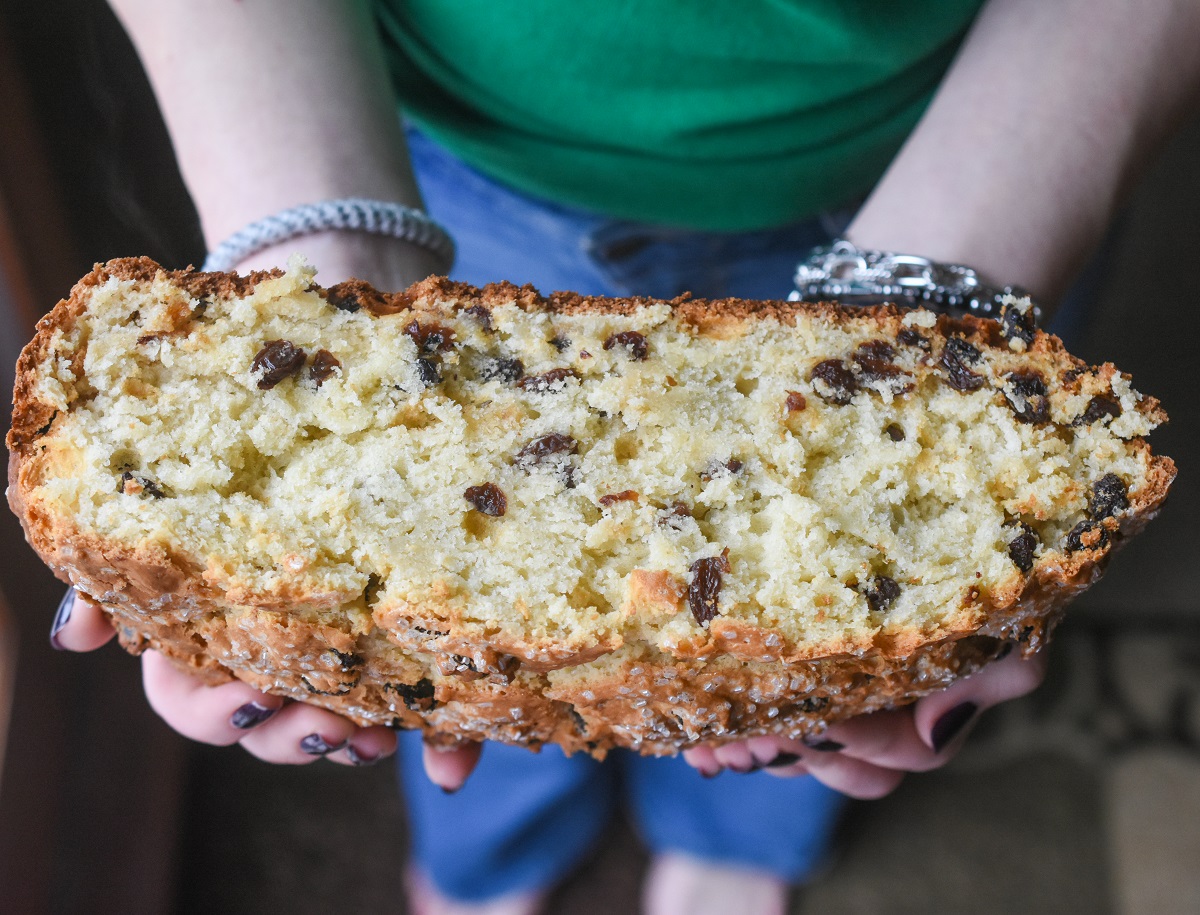 A big loaf of Irish Soda Bread with raisins cut in half being held in 2 hands. The very best Irish Soda Bread recipe.