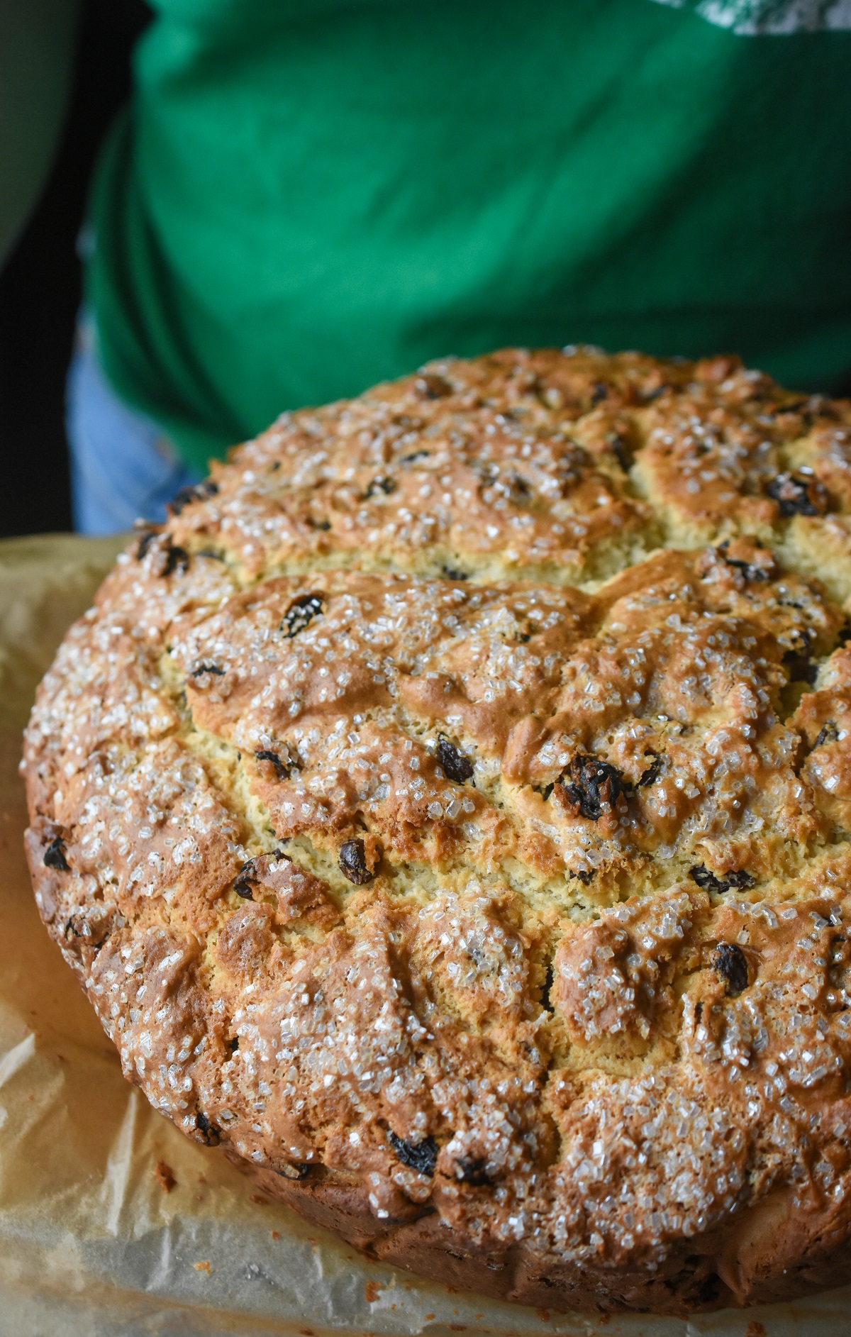 A big loaf of Sweet Irish Soda Bread with raisins dusted with sugar on parchment paper. The best Irish Soda Bread Recipe 