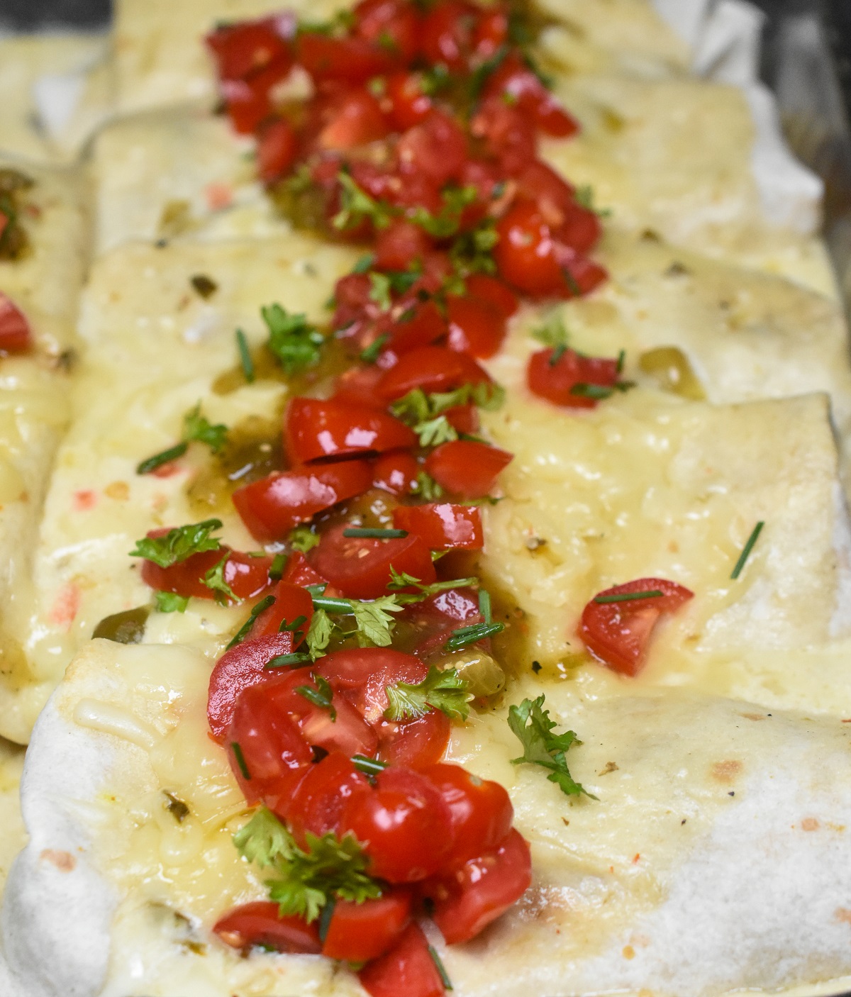 White Chicken Enchiladas in a pan sauce overtop garnished with chopped seasoned tomatoes and herbs