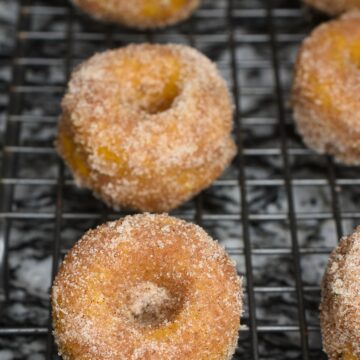 Baked Pumpkin Donuts coated in cinnamon sugar shown on wire rack. Pumpkin Spice Donuts