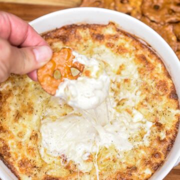 Hot Onion DIp Recipe! Onion Souffle Dip. Vidalia Onion DIp. shown baked in white disp with a pretzle scooping up some of the hot cheesey dip.