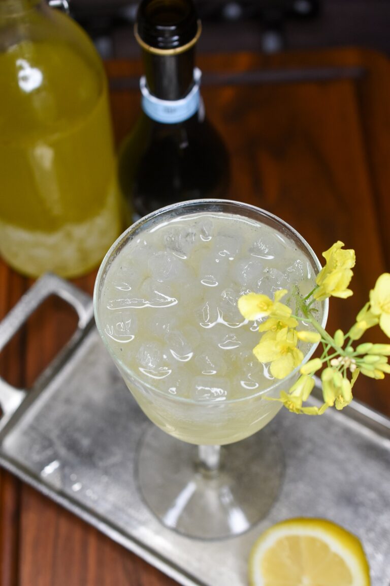 Limoncello Spritz recipe shown in vintage glass garnished with yellow flowers.