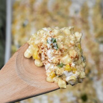 Mexican Street Corn Casserole is a delicious fresh corn recipe! Serve warm or room temperature. Can also be served as a Mexican Street Corn Dip. Shown on a wooden spoon over a white casserole dish