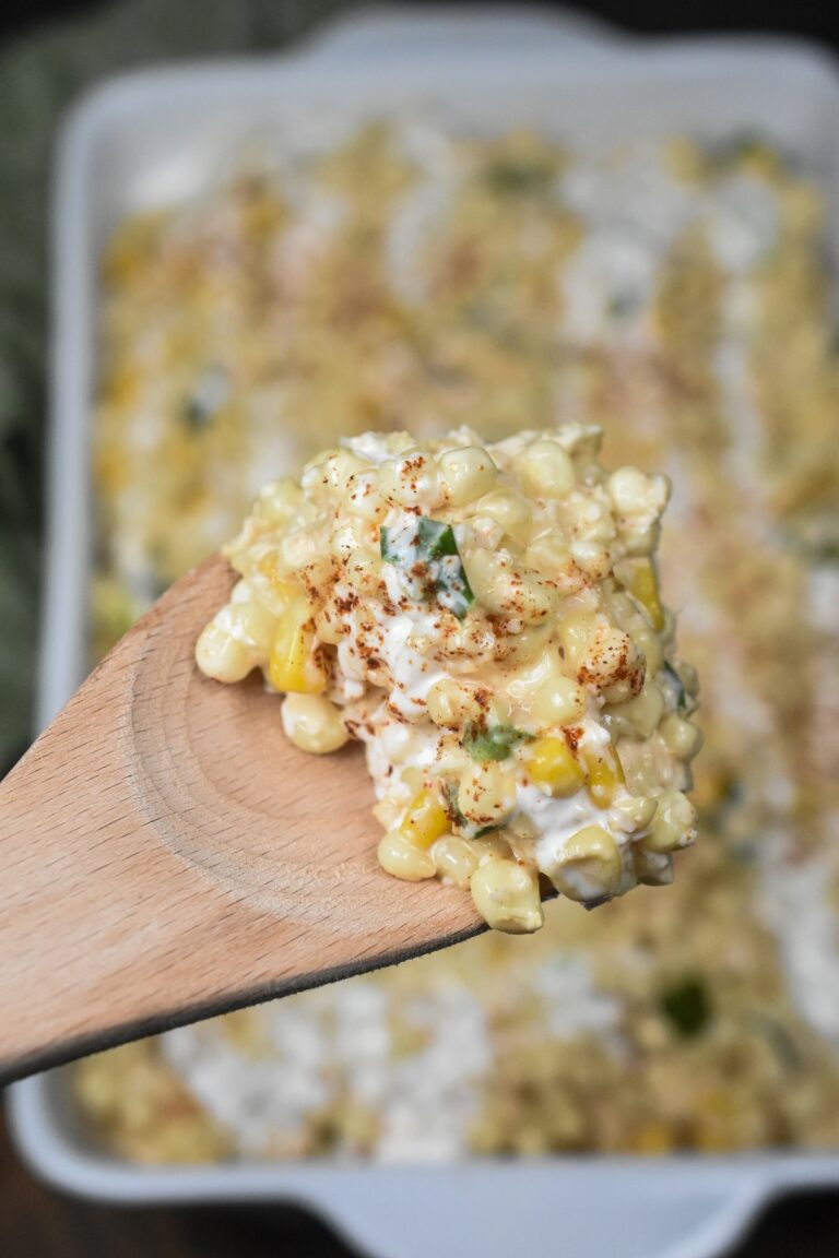 Mexican Street Corn Casserole is a delicious fresh corn recipe! Serve warm or room temperature. Can also be served as a Mexican Street Corn Dip. Shown on a wooden spoon over a white casserole dish