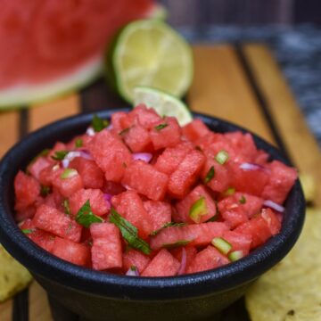 Watermelon Salsa shown in a black salsa bowl surrounded by tortilla chips
