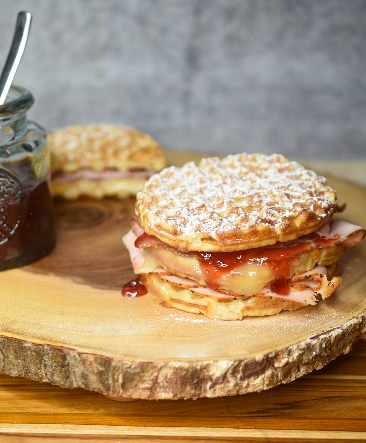 Monte Cristo Waffle Sandwich dusted with powdered sugar with homemade strawberry jam shown on a wood board.