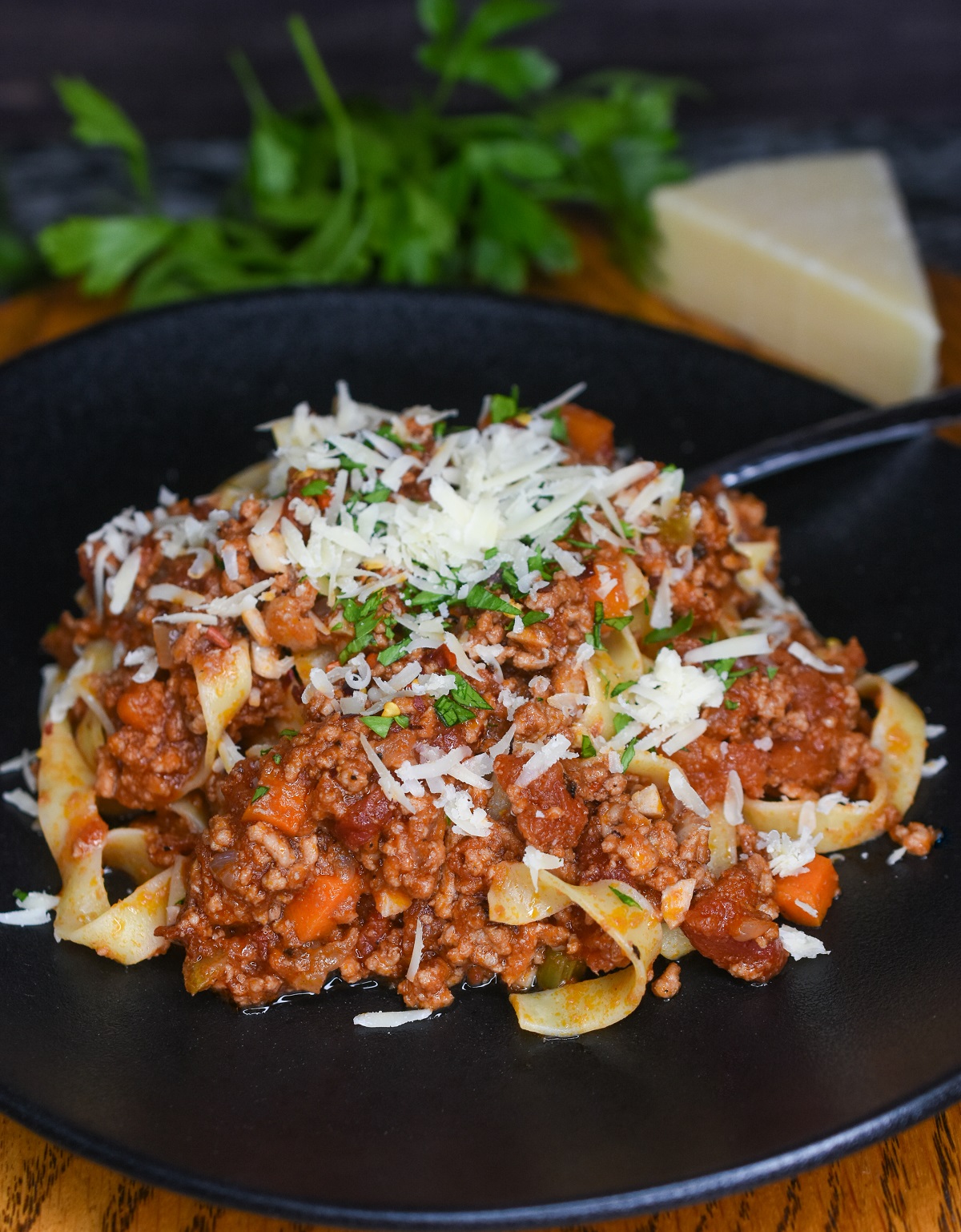 Pasta with bolognese sauce garnished with shredded cheese and herbs on a black plate.