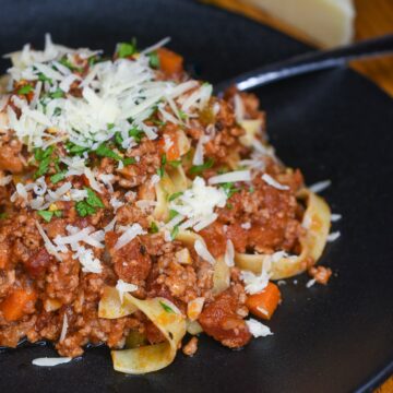 VEal Bolognese over pasta noodles garnished with shredded Parmesan and herbs.