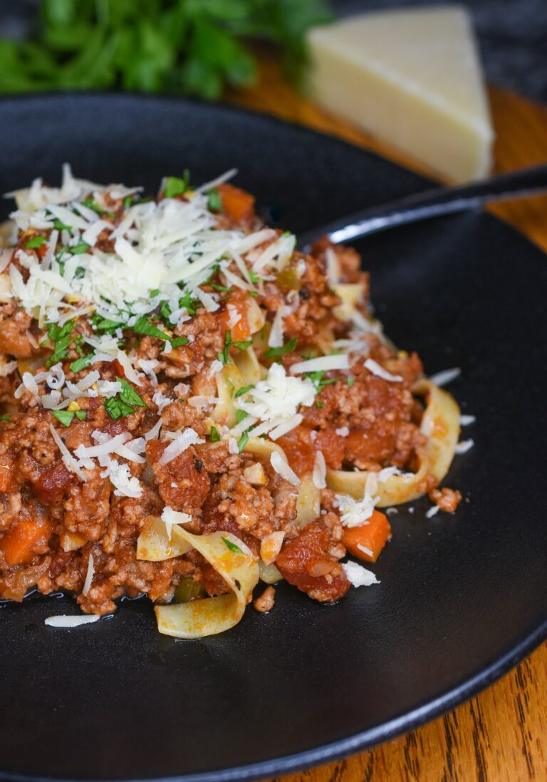 VEal Bolognese over pasta noodles garnished with shredded Parmesan and herbs.