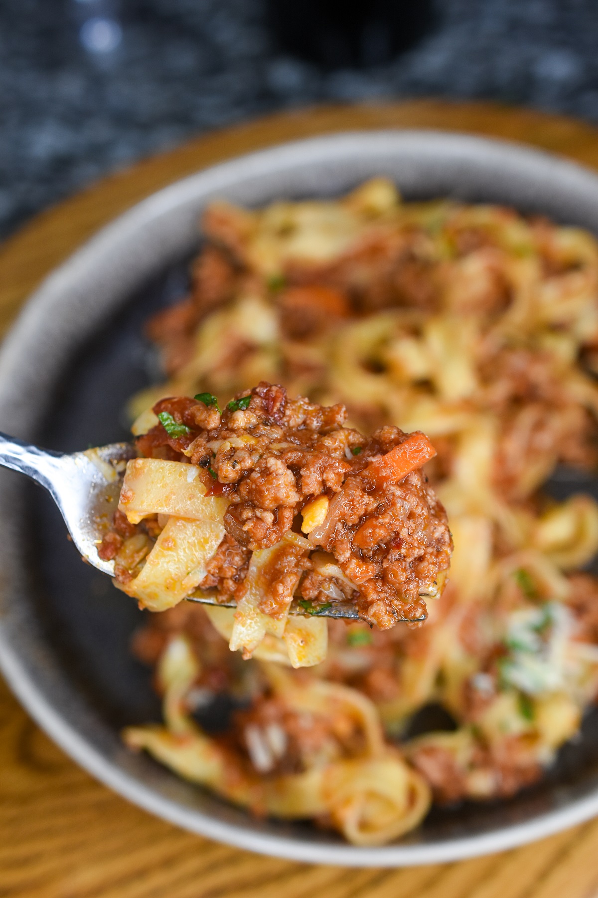 Bolognese and pasta noodles on a fork over a bowl full.