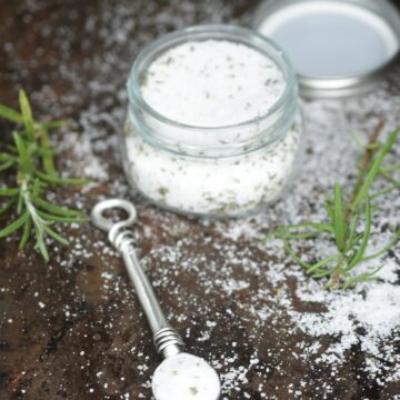 Homemade Rosemary Salt shown in small mason jar with sprigs of fresh Rosemary and a measuring spoon