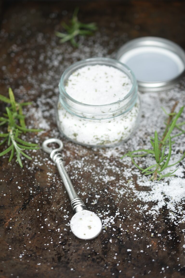 Homemade Rosemary Salt shown in small mason jar with sprigs of fresh Rosemary and a measuring spoon