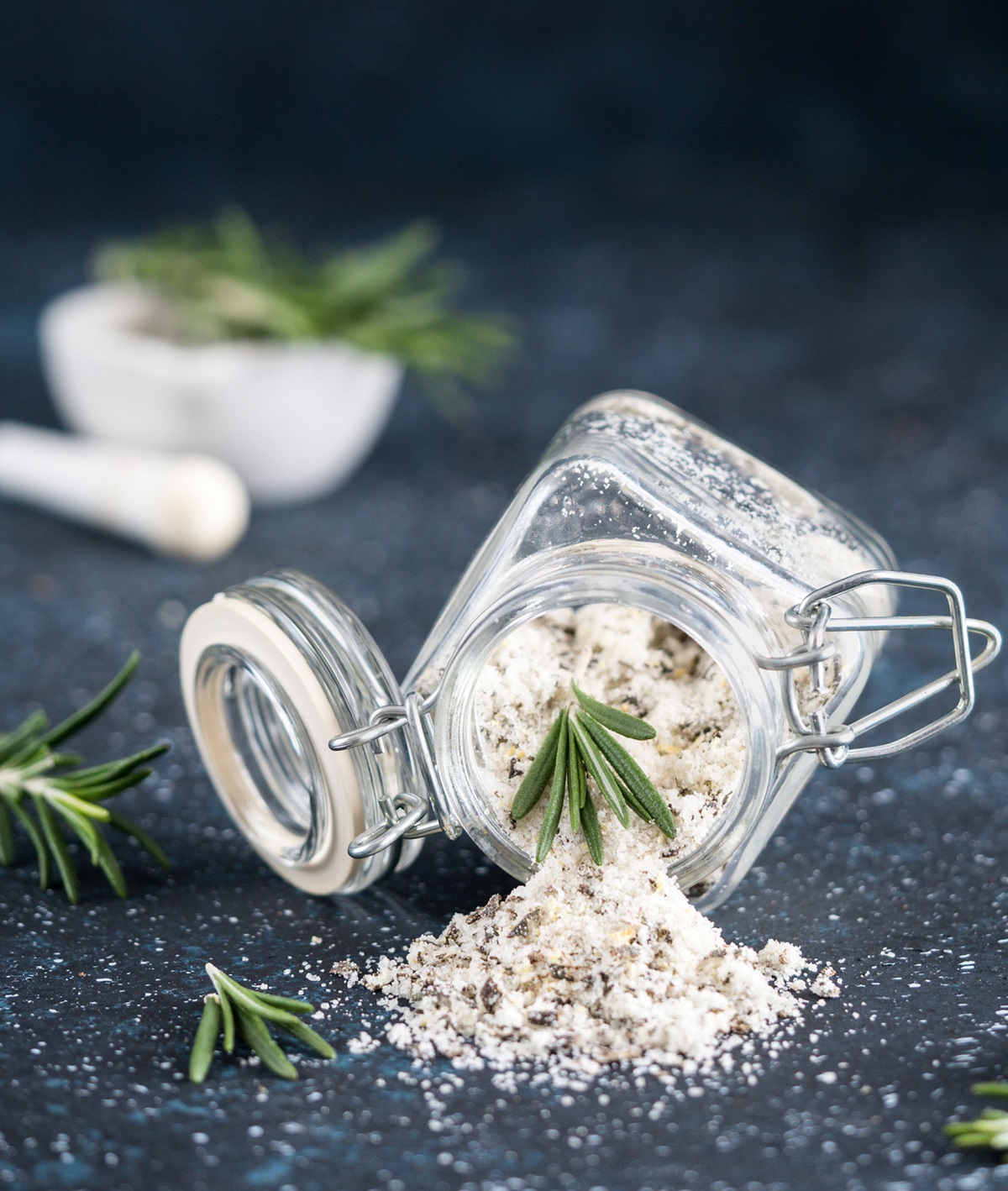 Truffle Salt with Rosemary, shown spilling out of a jar with sprigs of fresh Rosemary