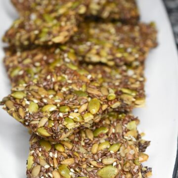 How to make seed crackers. Easy recipe for flourless crackers. Seed crackers made of sunflower seeds, pumpkin seeds, flax seeds, chia seeds and sesame seeds. Shown on white plate.