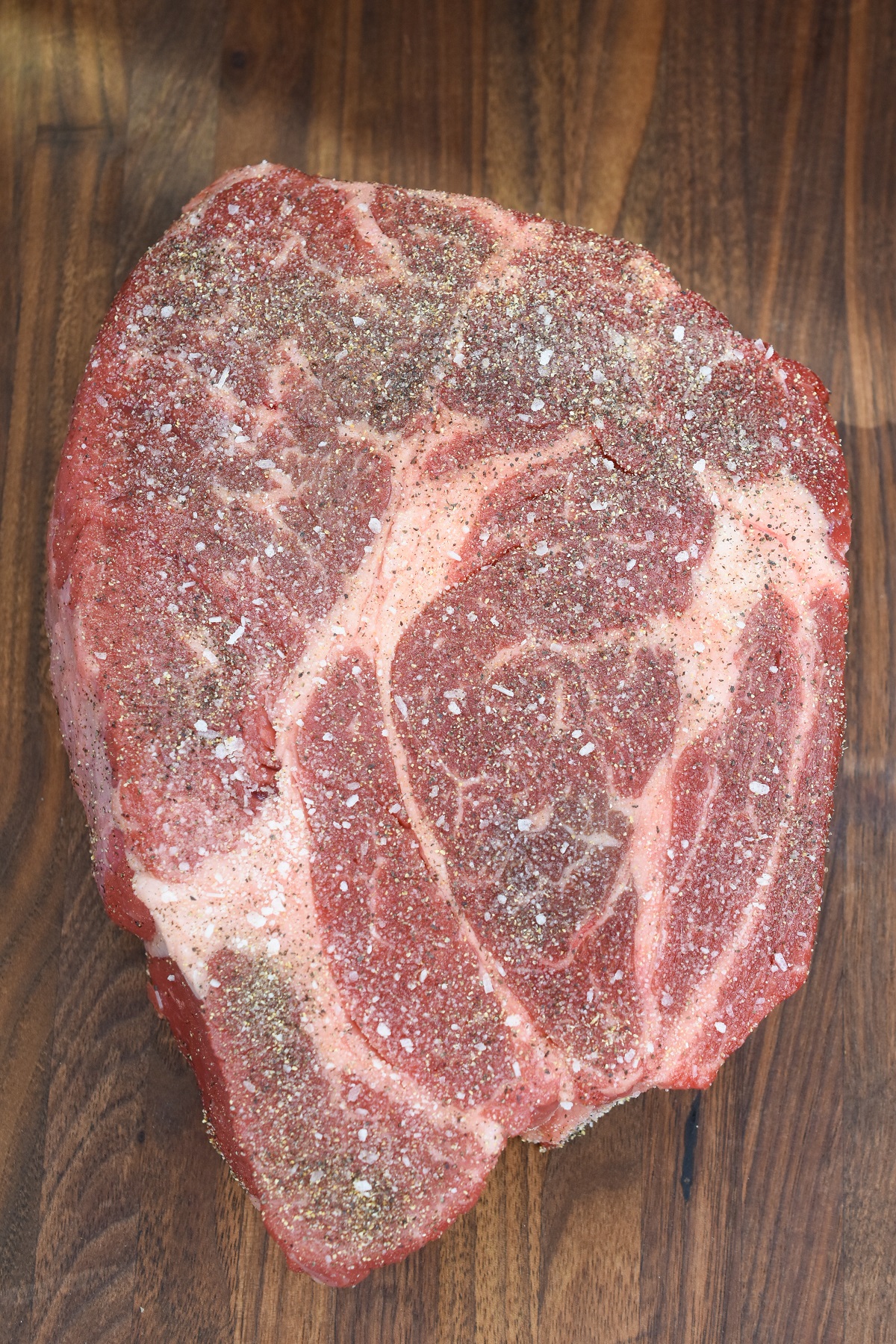 Raw chuck roast seasoned well with kosher salt and pepper on wood cutting board