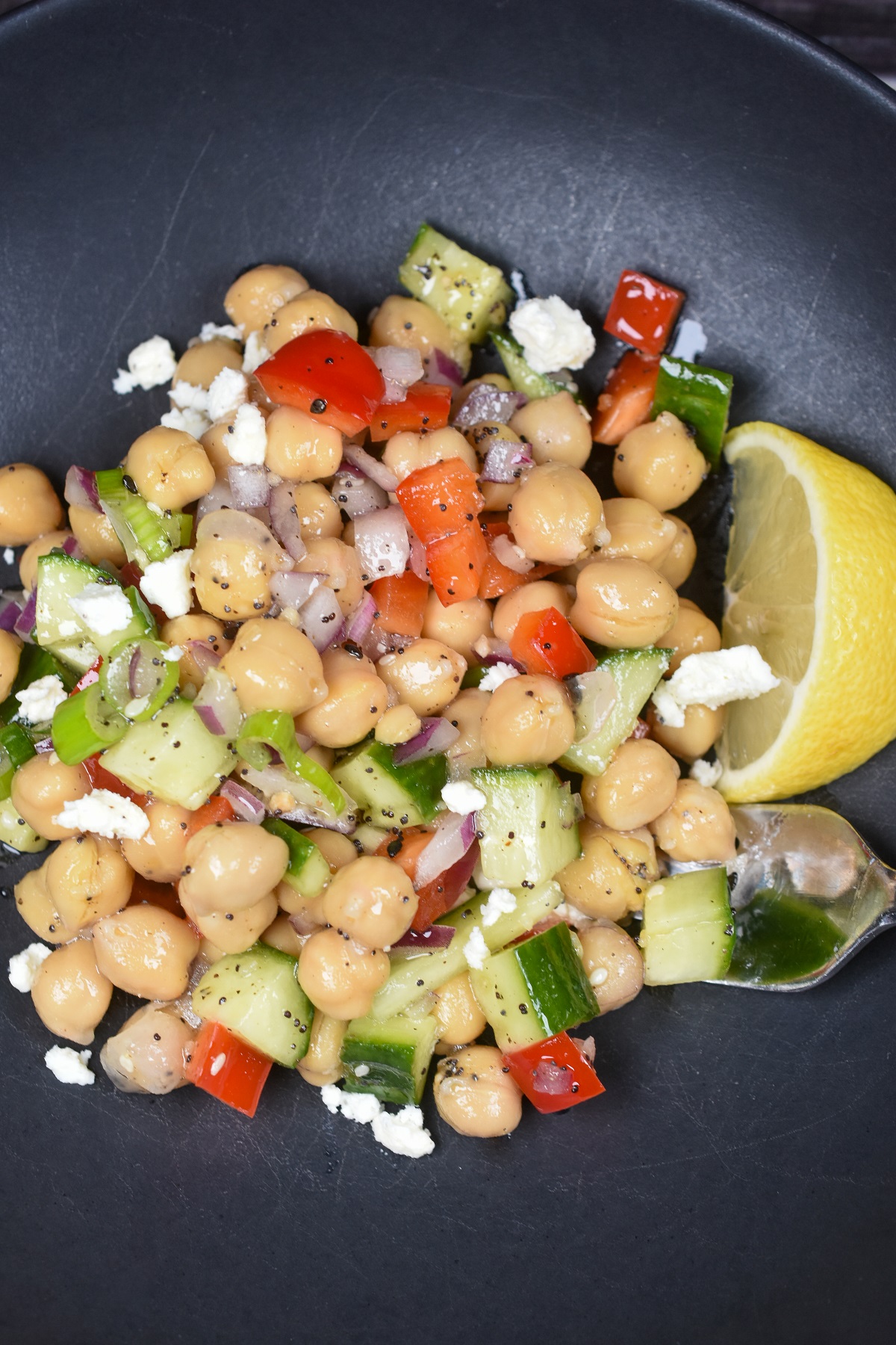 Chickpea Salad shown on plate with lemon wedge. Includes cucumbers, feta cheese, chickpeas, red pepper, red onion and parsley.