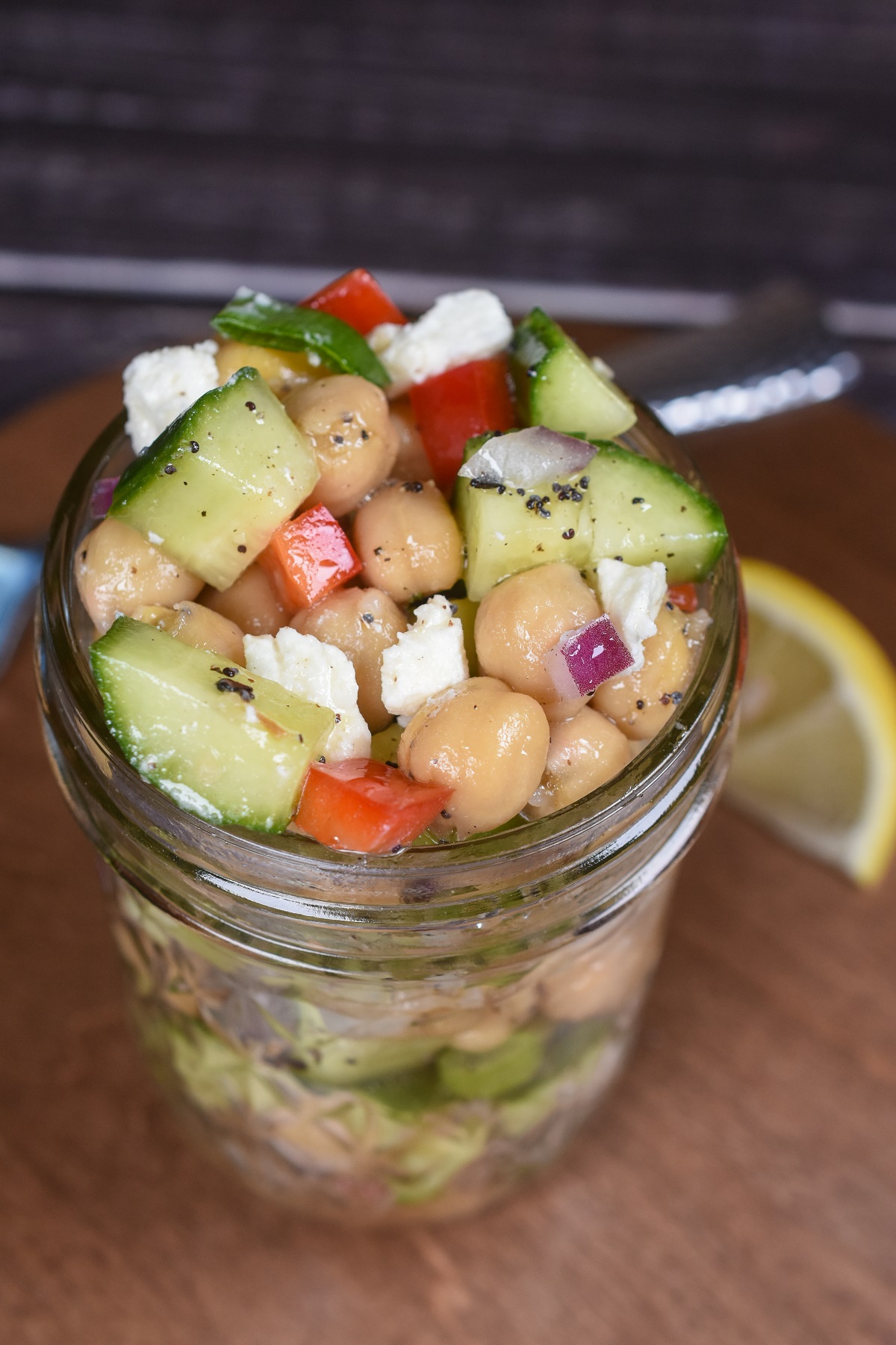 Dense Bean Salad recipe shown in mason jar. Make ahead bean salad for work lunch. Shown in salad in jar are chickpeas, feta, cucumbers, red onion and red peppers.