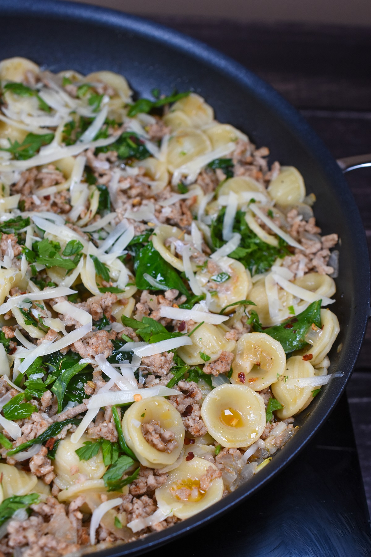 Orecchiette Pasta recipe. Pasta with ground veal and spinach. A flavorful pasta dish that is pure comfort food! Shown in a large skillet topped with Parmesan cheese and red pepper flakes.