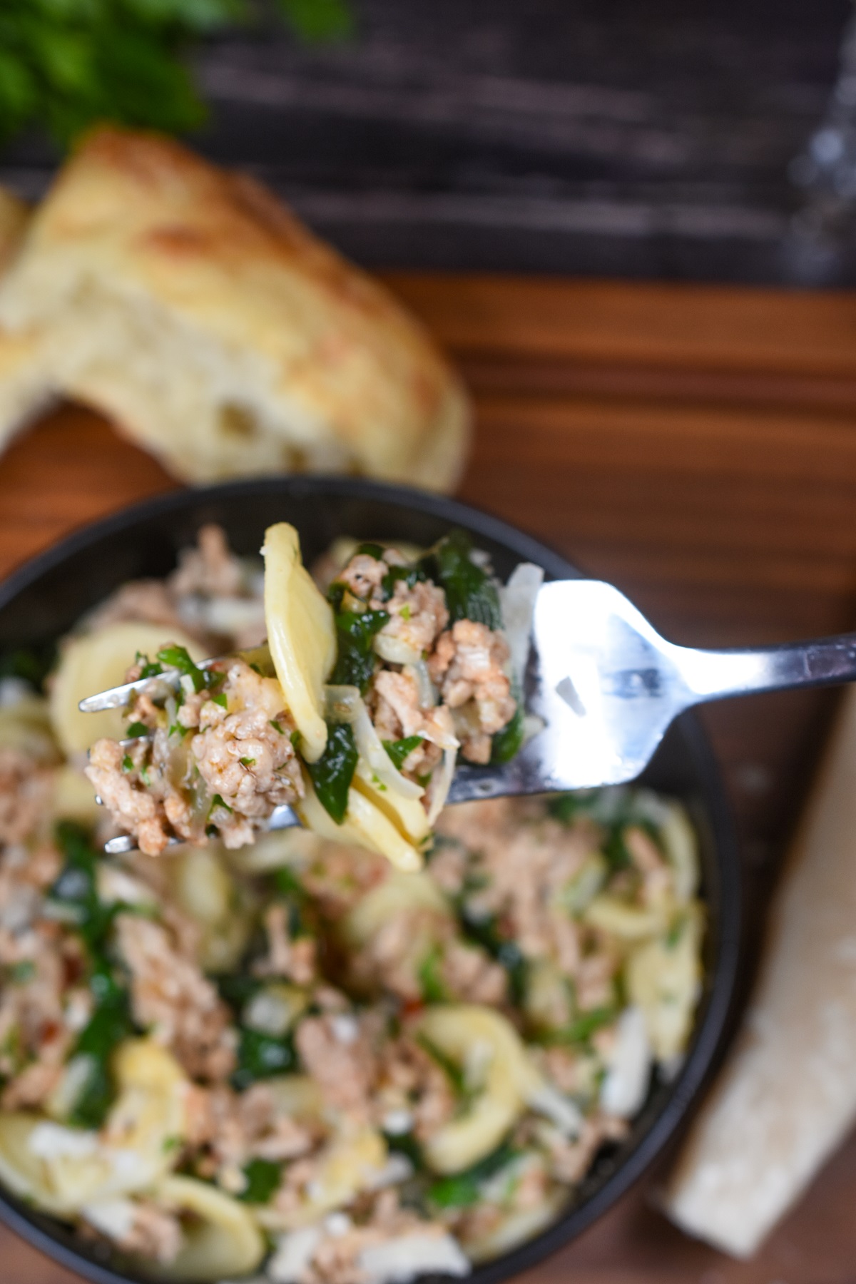 Orecchiette Pasta recipe. Pasta with ground veal and spinach. A flavorful pasta dish that is pure comfort food! Ground veal recipes. Shown on a fork over a bowl full or pasta and meat with spinach.