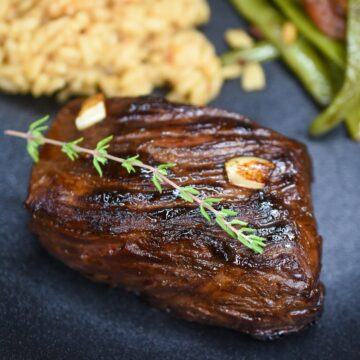 Bavette Steak cooked also called flap steak or bavette d boeuf shown on a black plate with farro and green beans