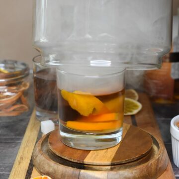 Smoked Old Fashioned shown with smoke overtop glass domw smoker.