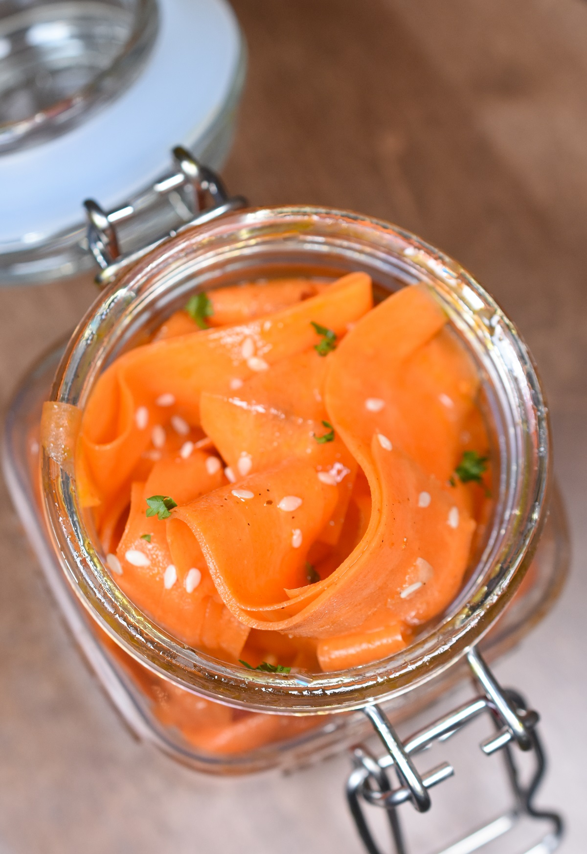 Korean Carrot Salad also called Morchovka is delicious and easy to make. Shown thin ribbons of carrot stored in a clear glass jar with lid. Garnished with parsley and sesame seeds