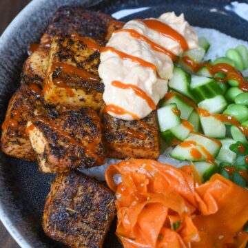 Salmon rice bowl shown with blackened salmon, rice, edamame, cucumbers, scallions and Korean carrot salad in black bowl