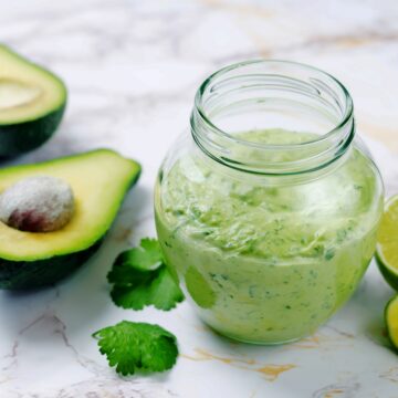 Avocado Crema shown in a jar alongside fresh avocado halves and a sliced lime