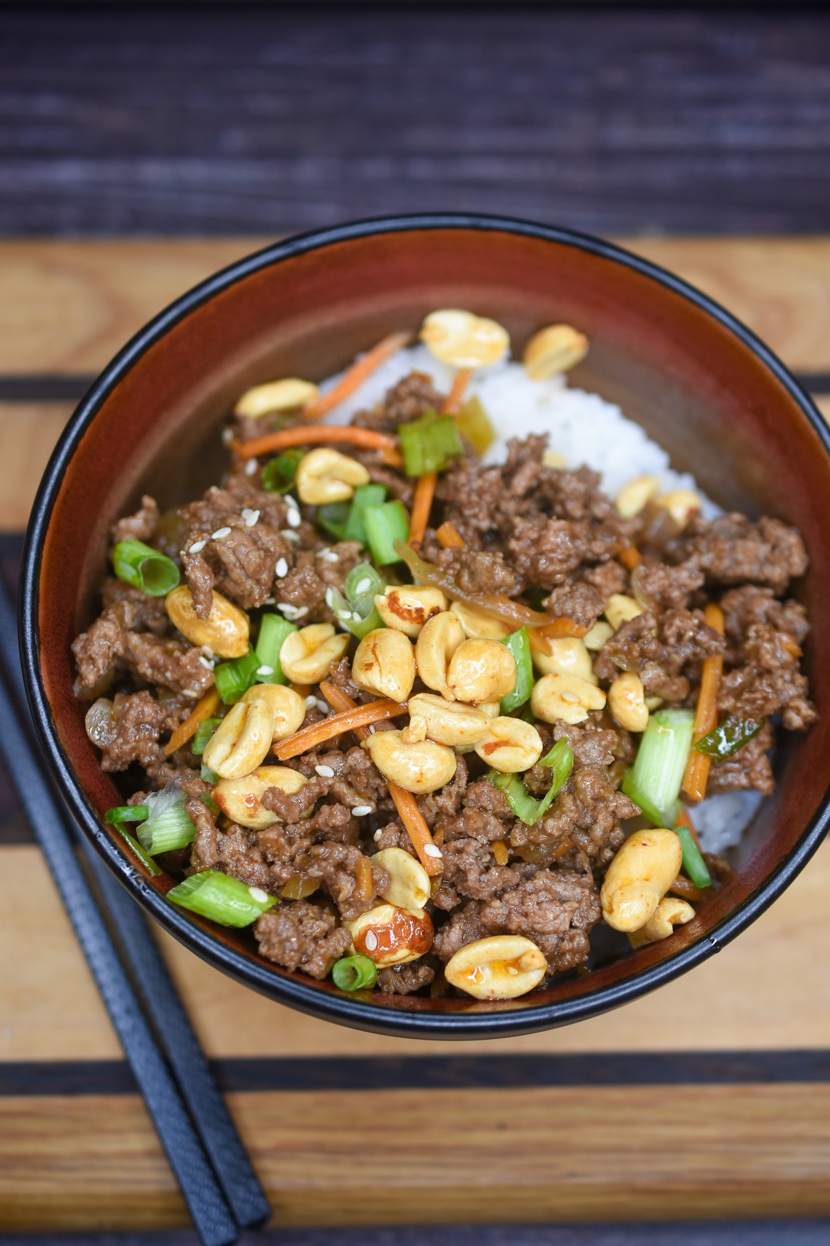 Ground Beef Stir Fry topped with peanuts shown in black bowl over sticky rice  with black chopsticks.