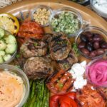 Mediterranean Platter Shown Grilled Kofta Kebabs on a large platter with roasted peppers, grilled asparagus and tomato halves, pita wedges, tzatziki. hummus, olives, crackers and pickled red onions