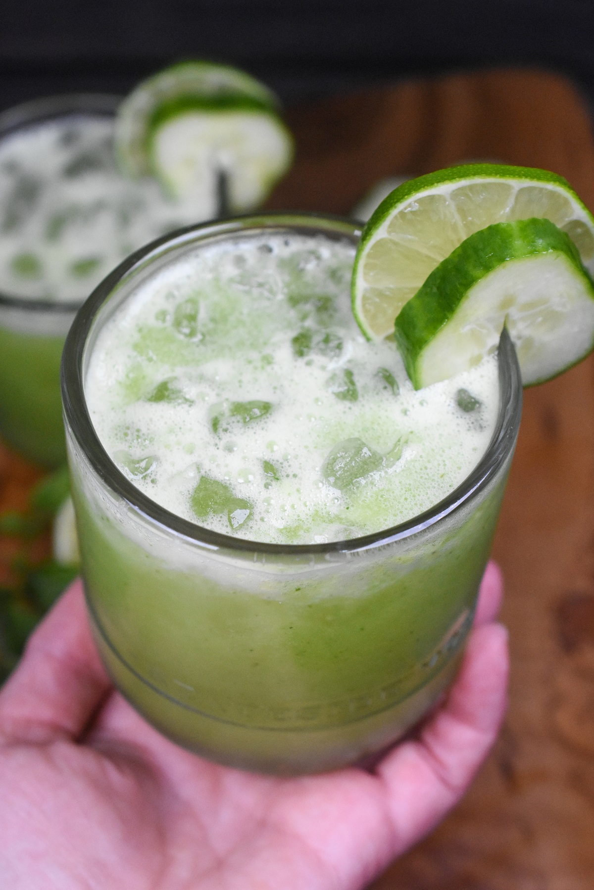Cucumber Agua Fresca Recipe. Super refreshing cucumber drink recipe. Aqua De Pepino is a delicious and easy way to stay hydrated. . Shown green juice in a clear glass held in a hand with ice. Sliced cucumbers and mint as rim garnish.