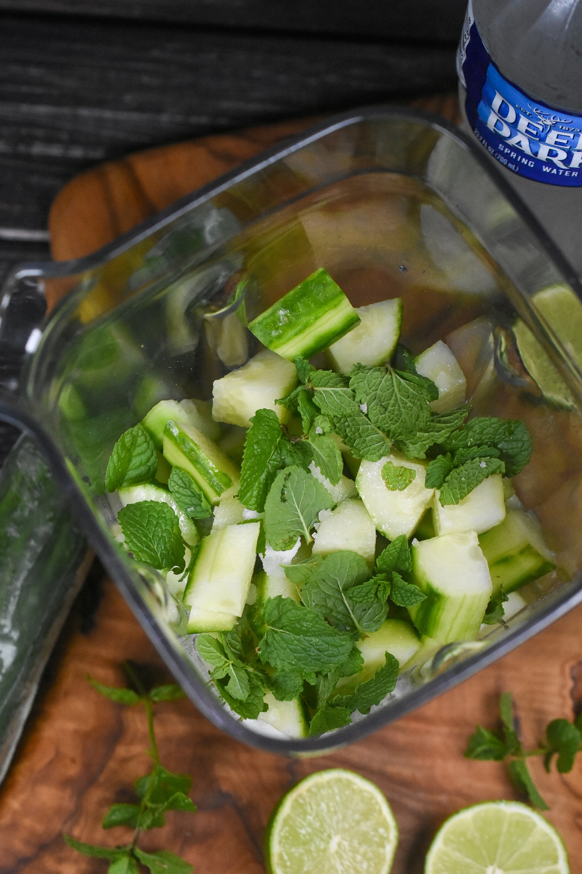 Ingredients to make a refreshing cucumber water drink called Agua De Fresca or Aqua De Pepino, its delicious and easy to make. Ingredients shown in a blender. Chopped cucumber, mint leaves, sugar and salt with bottle of water in background.