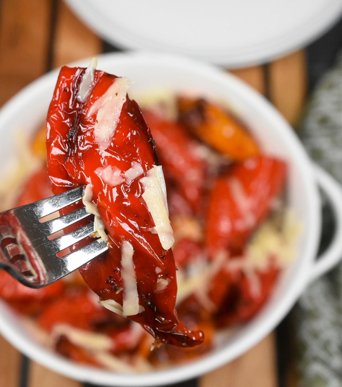 Mini Sweet Peppers cooked in the air fryer. Air Fryer Peppers are a fabulous snack, light meal, tapas dish or charcuterie board addition. Shown in a white bowl with shaved Parmesan on top of the peppers, with one pepper held above bowl by a fork