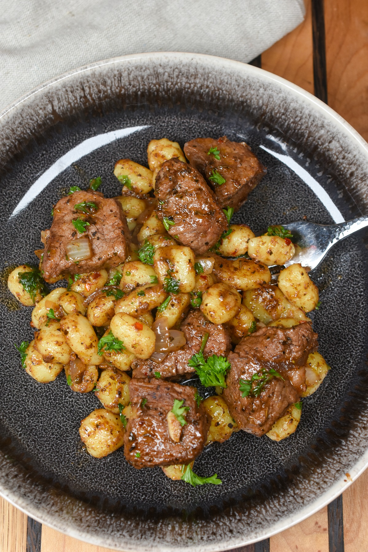 Steak Bites with Potato Gnocchi in a black dish garnished with fresh parsley