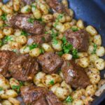steak bites with potato gnocchi shown in a pan garnished with fresh parsley.