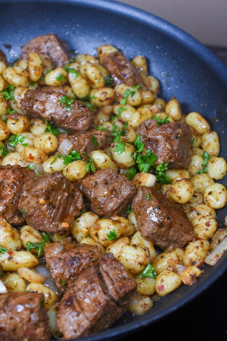 steak bites with potato gnocchi shown in a pan garnished with fresh parsley.