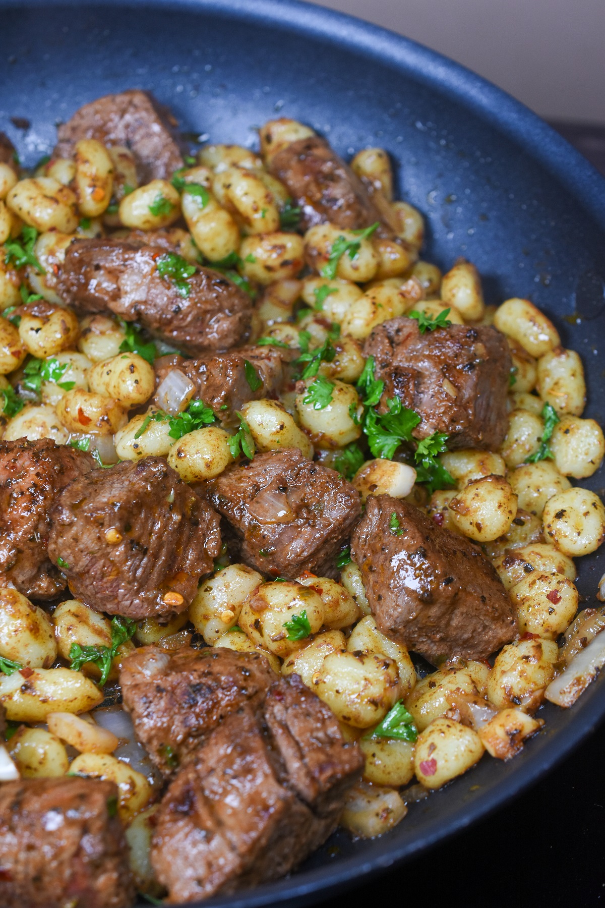 Beef Tenderloin Steak Bites and Potato Gnocchi cooked in pan garnished with fresh parsley.