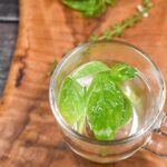 Fresh Basil tea in a clear glass mug on a wood cutting board with fresh basil in background