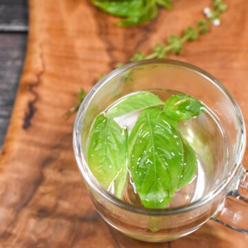 Fresh Basil tea in a clear glass mug on a wood cutting board with fresh basil in background